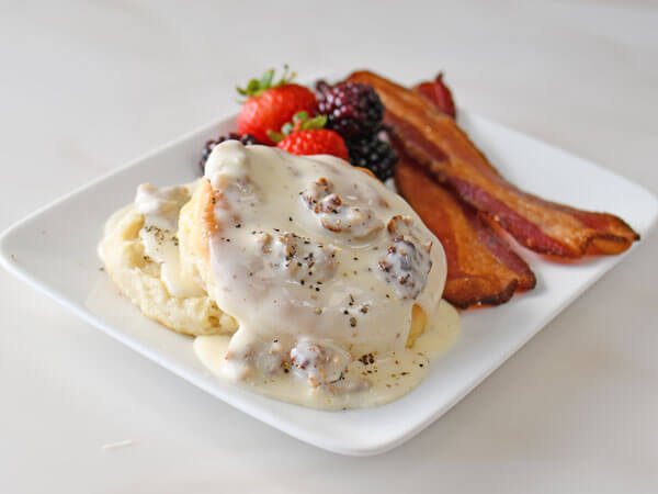A plate of sausage gravy with biscuits and bacon