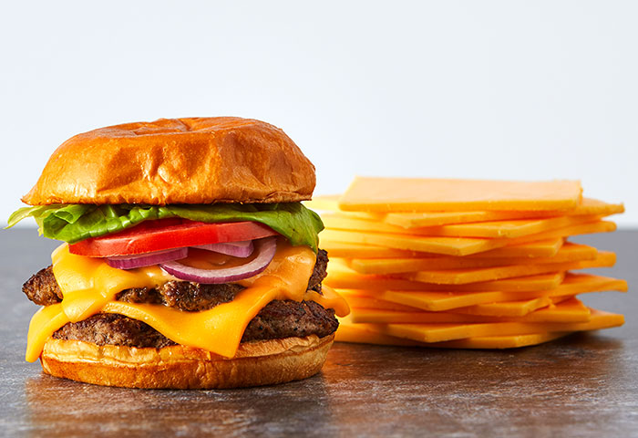 Photo of a double cheeseburger with lettuce, tomato, red onion and Land O Lakes Extra Melt® Sharp American Cheese Slices melted.